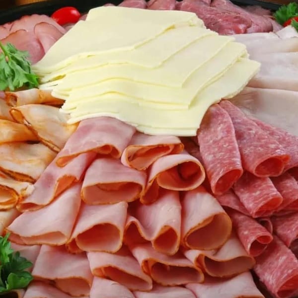 A European deli platter with various sliced meats, cheeses, and garnishes.